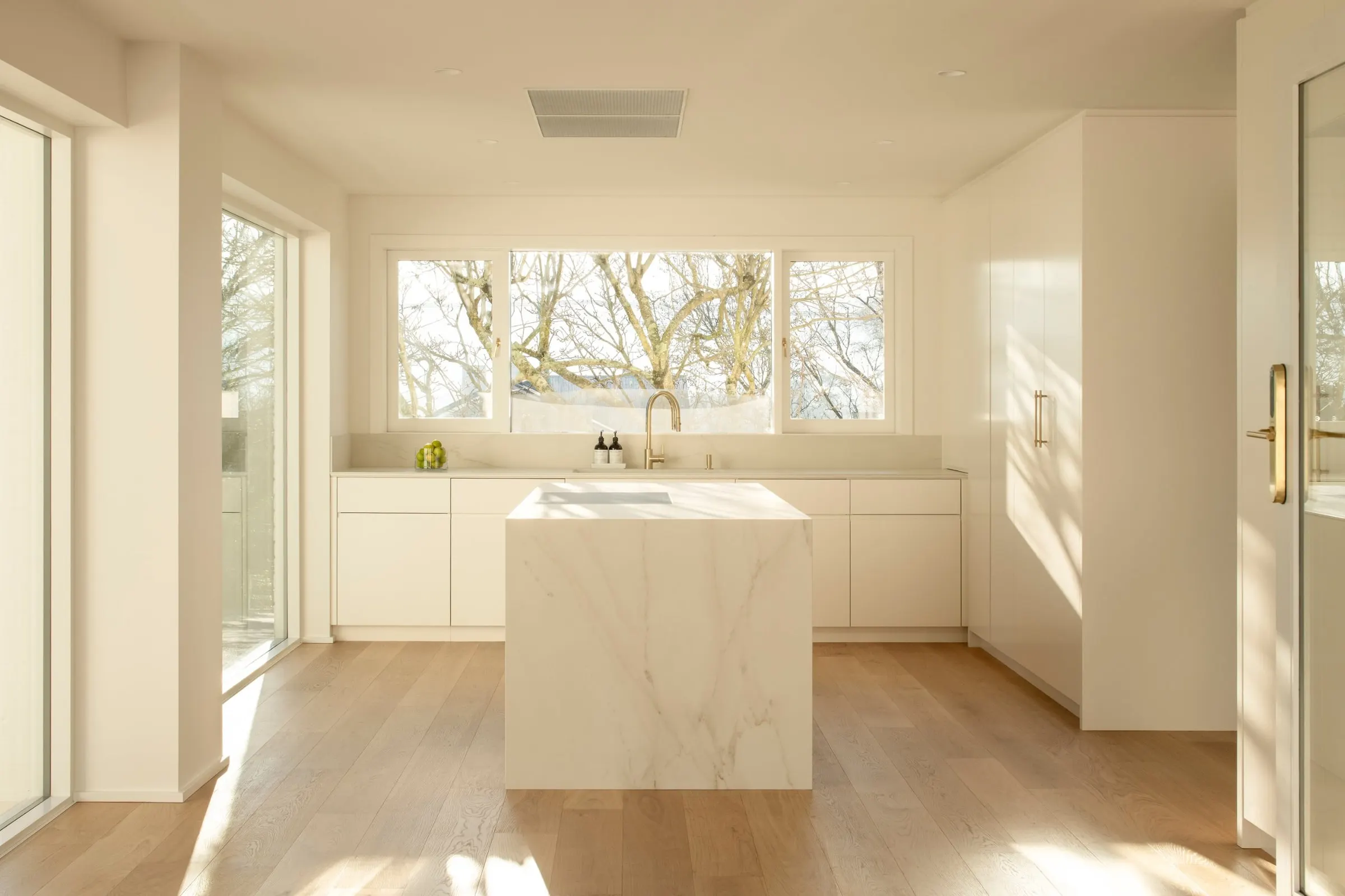 A finished kitchen with a stone island, white joinery and oak floors in low sun, Newstead