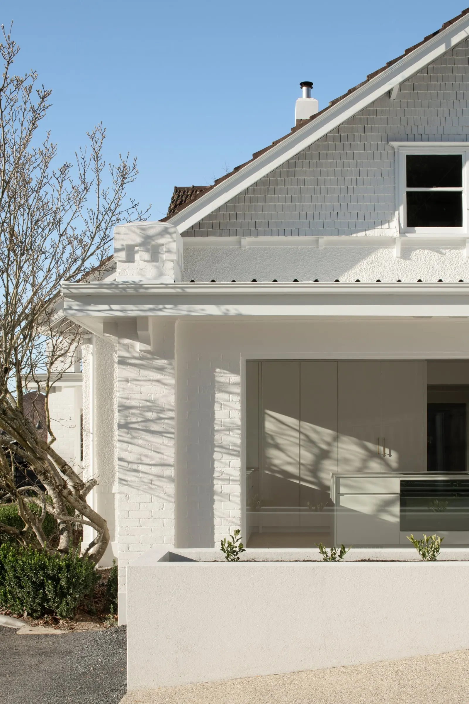 Close view of the painted brick piers and shingled gable of a finished house, Newstead